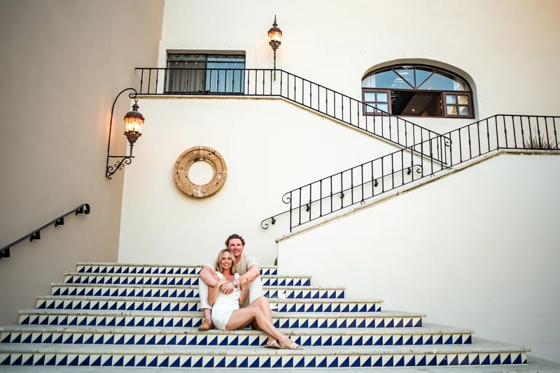 Jacquelyn and Jake seated on the tiled staircase at Zoëtry Casa del Mar, beneath its wrought-iron railings